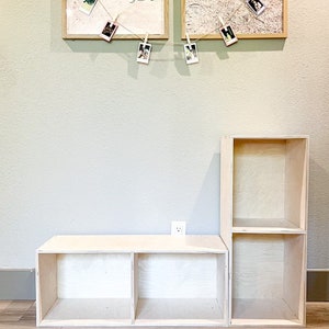 May include: A set of two unfinished wooden shelves with three compartments each. The shelves are made of plywood and have a natural wood finish. The shelves are stacked on top of each other, with the larger shelf on the bottom. The shelves are empty and ready to be decorated.