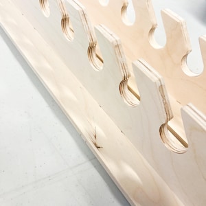 May include: A wooden shelf with multiple cutouts for holding tools or other items. The shelf is made of light-colored wood and has a natural finish.