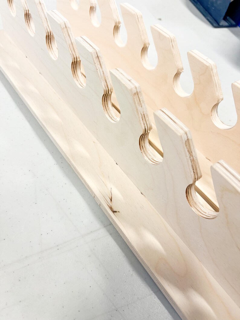 May include: A wooden shelf with multiple cutouts for holding tools or other items. The shelf is made of light-colored wood and has a natural finish.