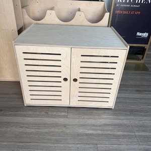 May include: A light-colored wooden cabinet with two doors featuring horizontal slats. The cabinet has a flat top and is part of a larger wooden structure. The cabinet is likely for storage.