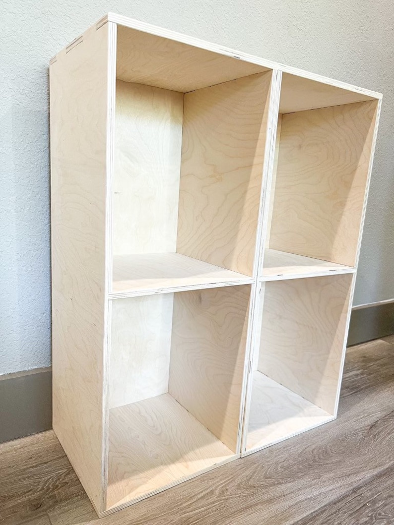 May include: A wooden shelf unit with four open compartments. The shelf is made of light-coloured wood and has a simple, modern design.