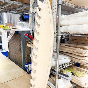 May include: A light wood shelf with multiple cutouts for holding items. The shelf is mounted to a pegboard wall and is labeled "Fish Tackle".