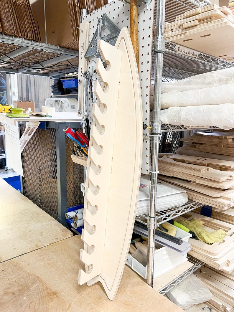 May include: A light wood shelf with multiple cutouts for holding items. The shelf is mounted to a pegboard wall and is labeled "Fish Tackle".