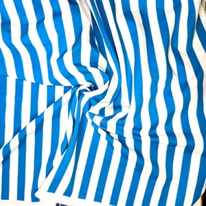 May include: A close-up shot of a fabric with vertical stripes in bright blue and white. The fabric is draped and folded, creating a textured effect. The stripes are evenly spaced and run the length of the material.