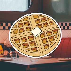 May include: A cartoon illustration of a waffle with a pat of butter on top. The waffle is brown and yellow and has a white outline. The background is a blurry image of a diner.