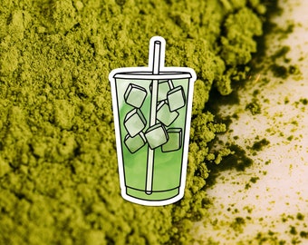 Può includere: Una bevanda al matcha verde ghiacciata con una cannuccia in un bicchiere di plastica trasparente. La bevanda è circondata da polvere di matcha verde.