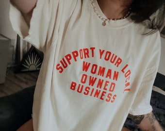 May include: A white t-shirt with the text "Support Your Local Woman Owned Business" printed in red.
