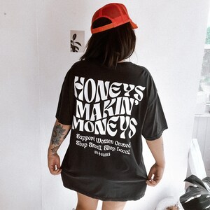May include: Black oversized t-shirt with white text that reads "Honeys Makin Moneys Support Women Owned Shop Small Shop Local. We Babes".