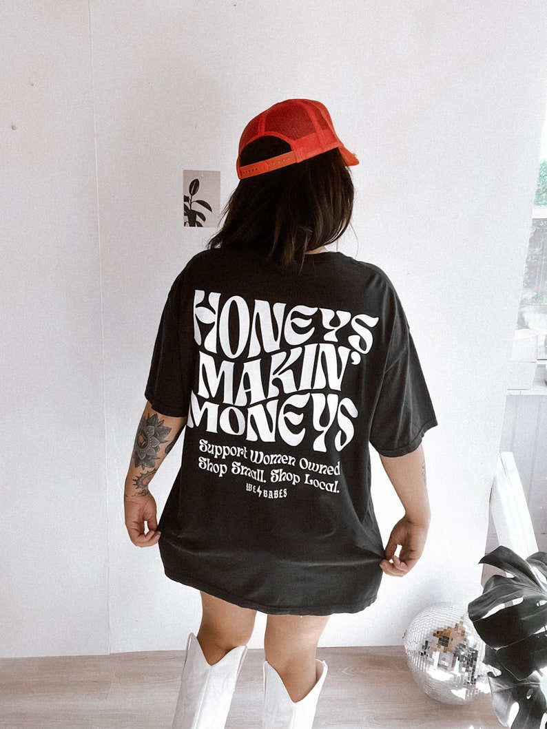 May include: Black oversized t-shirt with white text that reads "Honeys Makin Moneys Support Women Owned Shop Small Shop Local. We Babes".