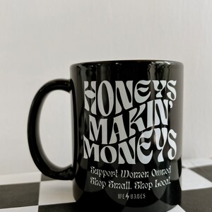 May include: Black ceramic mug with white text that reads "Honeys Makin Moneys" and "Support Women Owned Shop Small. Shop Local. We 4 Babes".