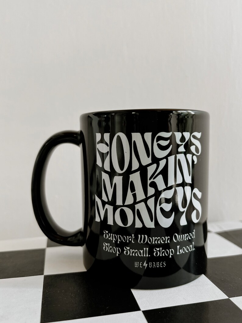 May include: Black ceramic mug with white text that reads "Honeys Makin Moneys" and "Support Women Owned Shop Small. Shop Local. We 4 Babes".