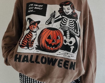 May include: Brown Halloween-themed sweatshirt with a graphic featuring a cat in a witch hat, a skeleton, and a carved pumpkin. The text reads "IT'S NEVER TOO EARLY FOR... HALLOWEEN."