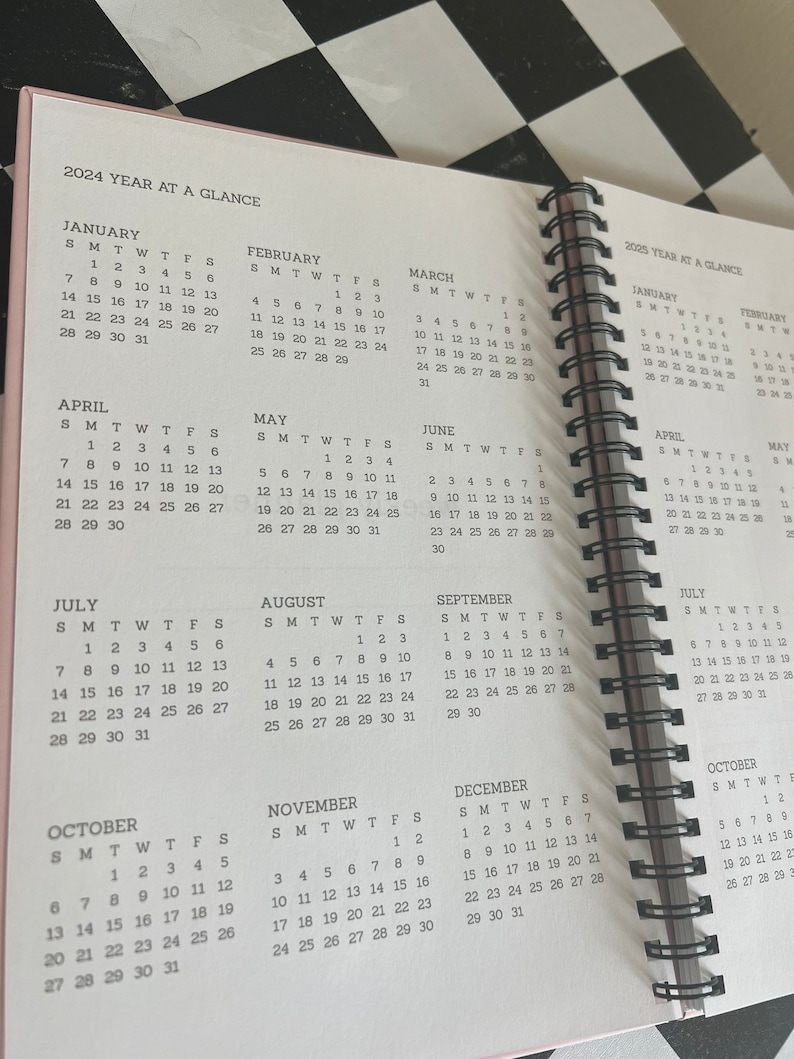 K&ouml;nnte beinhalten: Ein rosa-farbener, spiralgebundener Planer, der Jahreskalender f&uuml;r 2024 und 2025 zeigt. Die Seiten zeigen Monatskalender mit Daten und Wochentagen, n&uuml;tzlich f&uuml;r die Planung.