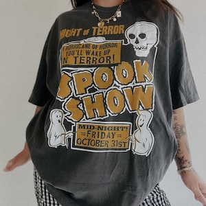 May include: A dark grey t-shirt with a graphic print of a spooky show announcement. The text reads "Night of Terror, Hurricane of Horror, You'll Wake Up in Terror! Spook Show, Mid-Night! =Friday= October 31st".