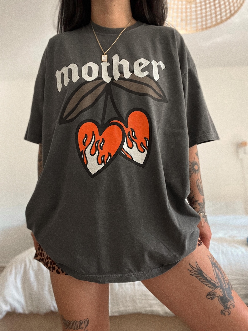 May include: A charcoal grey oversized t-shirt with a graphic print of two red hearts with flames on a stem with leaves. The text "mother" is printed above the hearts.