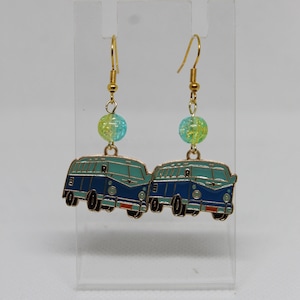 May include: A pair of dangle earrings featuring blue and teal camper van charms with gold-colored accents. Each earring has a translucent, yellow-green bead and gold-colored fish hook. The earrings are displayed against a white background.