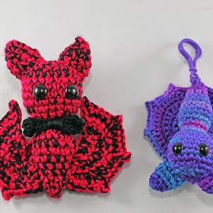 May include: Two crocheted bats, one red and black with a black bow tie, and one purple and blue with a purple keychain loop.