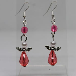 May include: A pair of silver angel earrings with pink and white beads. The angel is holding a pink crystal.