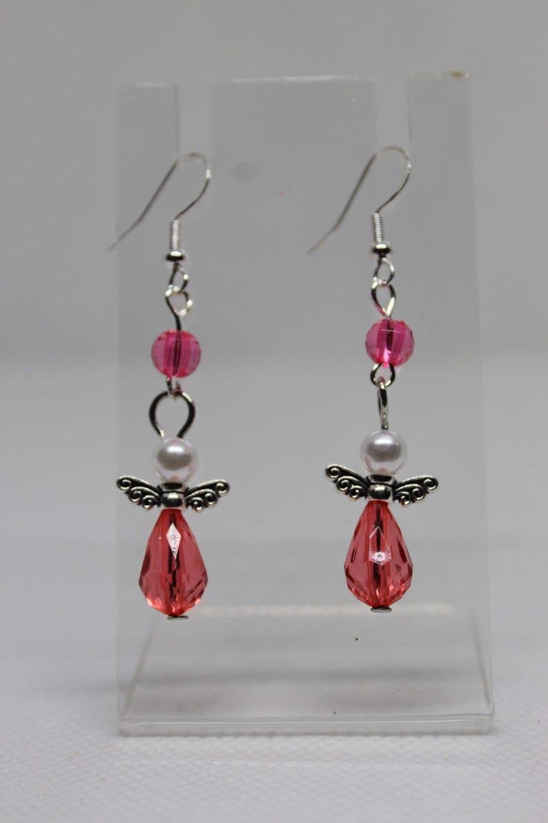 May include: A pair of silver angel earrings with pink and white beads. The angel is holding a pink crystal.