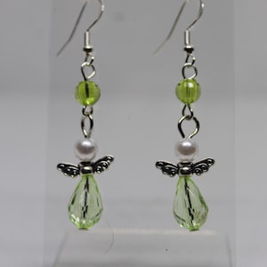 May include: A pair of dangle earrings with silver angel charms, white pearl beads, and light green faceted glass beads.