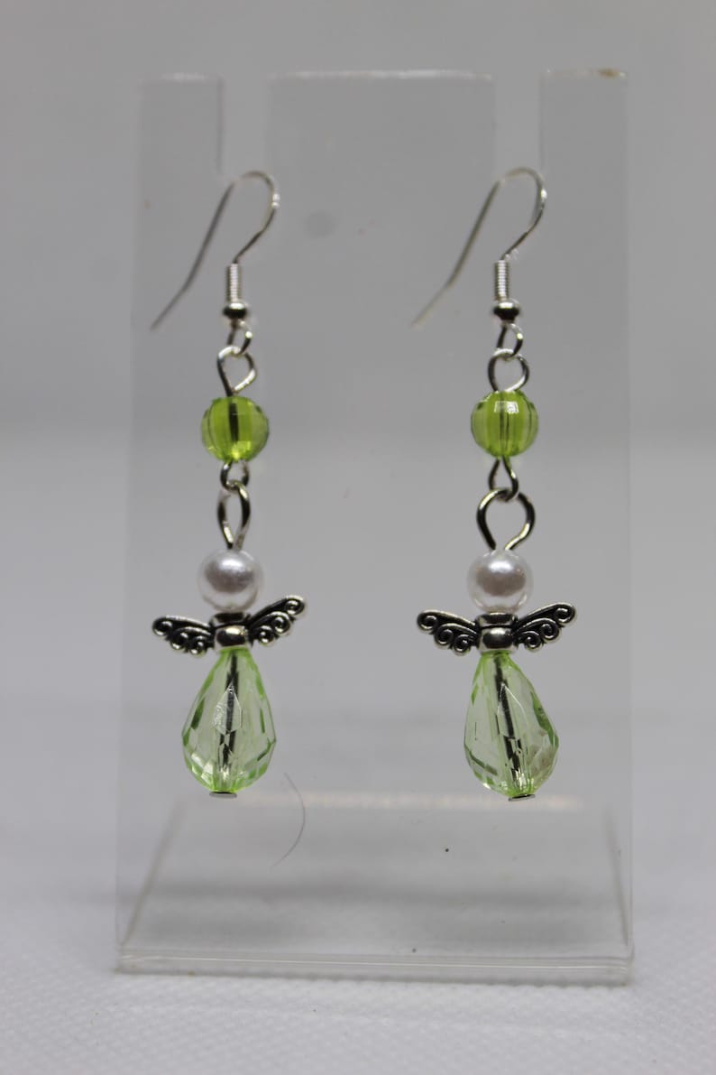 May include: A pair of dangle earrings with silver angel charms, white pearl beads, and light green faceted glass beads.