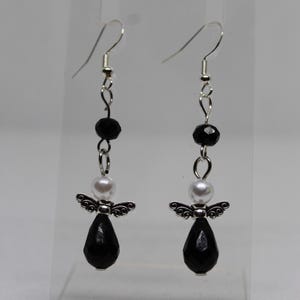 May include: A pair of dangle earrings with black and white beads and silver angel charms. The earrings have a teardrop-shaped black bead at the bottom.