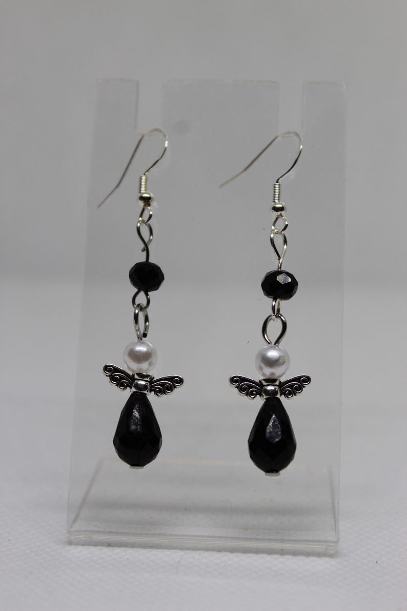 May include: A pair of dangle earrings with black and white beads and silver angel charms. The earrings have a teardrop-shaped black bead at the bottom.