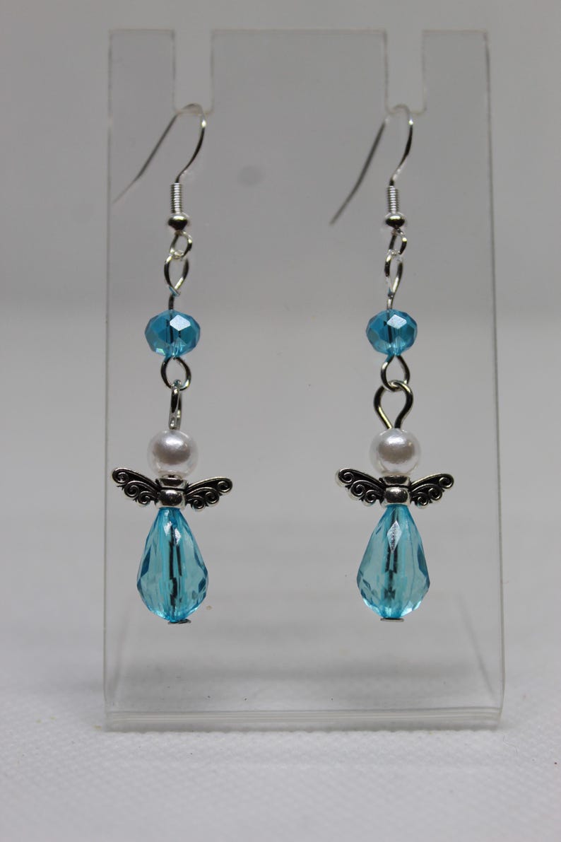 May include: A pair of dangle earrings featuring a silver angel charm with a light blue crystal teardrop, a white pearl bead, and a light blue crystal bead.