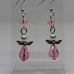 May include: Pink and white angel dangle earrings with crystal drops. The earrings are silver-toned and feature a small pearl bead.