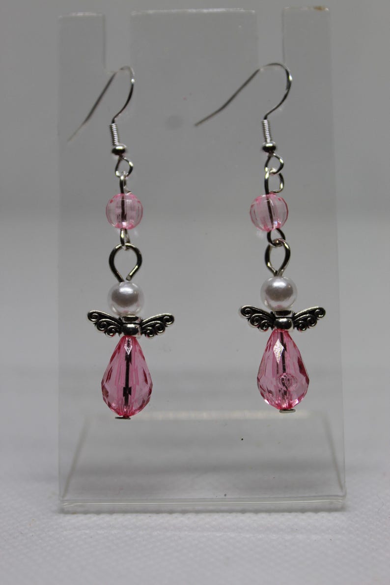 May include: Pink and white angel dangle earrings with crystal drops. The earrings are silver-toned and feature a small pearl bead.