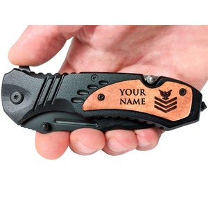 May include: Black folding pocket knife with a wood handle. The handle has a personalized inscription that reads "YOUR NAME" and a small eagle insignia.
