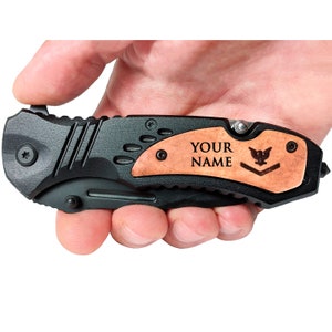 May include: A black folding knife with a wood handle. The handle has a personalized inscription that says "YOUR NAME" and a small eagle design.