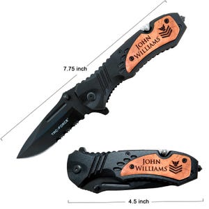 May include: A black folding knife with a wood handle. The handle is engraved with the name "JOHN WILLIAMS" and a military insignia. The knife is 7.75 inches long and 4.5 inches when closed. The knife is made by TRC-FORCE.
