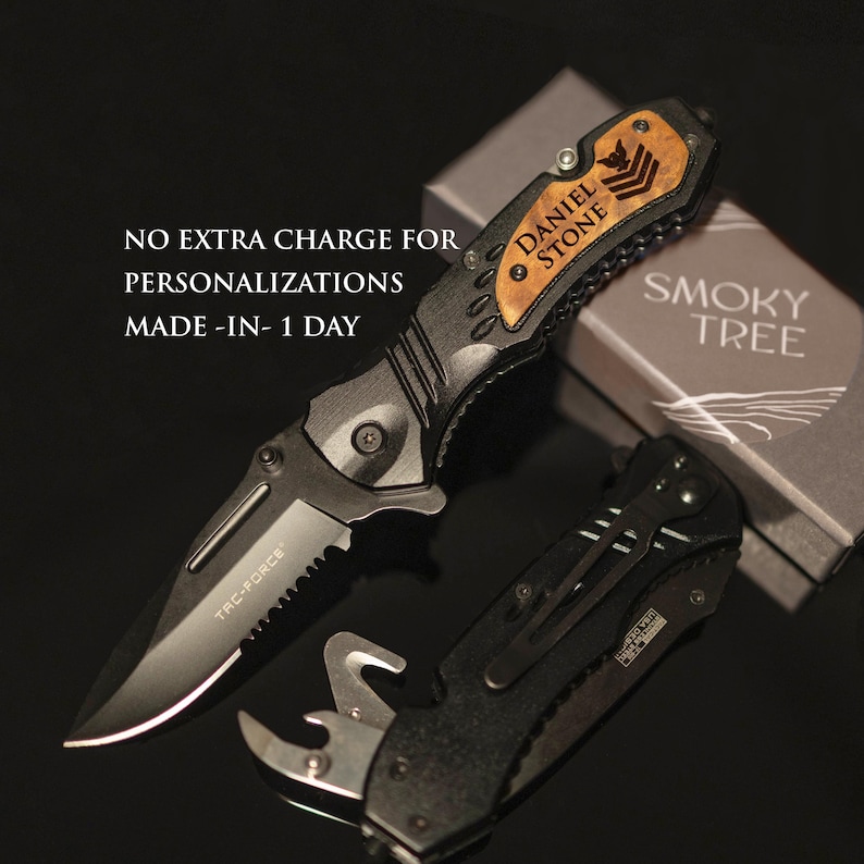 May include: A black folding knife with a wood handle engraved with the name "Daniel Stone". The knife is open and the blade is visible. The knife is in a box with the words "Smoky Tree" printed on it.