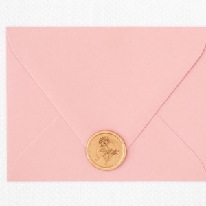 May include: A pink envelope with a gold wax seal featuring a floral design.