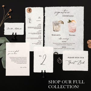 May include: A wedding stationery set with a rustic, vintage aesthetic. The stationery includes a table number card, a sign for guests to sign, and a menu card. The cards are printed on textured paper with a distressed look. The table number card is a simple design with the number "2" written in black ink. The sign for guests to sign is a simple design with the words "Please sign our Guest Book" written in black ink. The menu card is a more elaborate design with a list of cocktails, wines, and beers. The cocktails are illustrated with watercolour paintings of margaritas and palomas. The menu card also includes the text "Signature Cocktails" and "Also Serving".