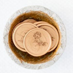 May include: A close-up of a bowl filled with gold wax seals featuring a floral design. The seals are stacked on top of each other and have a subtle shimmer.