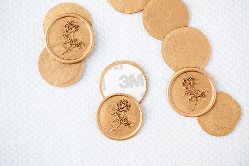 May include: Gold wax seals with a floral design. The seals are on a white surface. Some of the seals have a 3M adhesive backing.