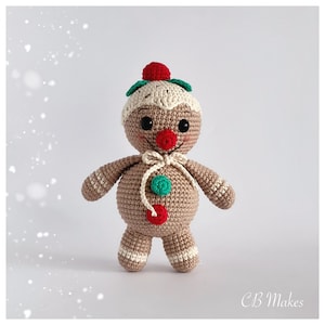 May include: A crocheted gingerbread man toy with a red and green hat, red buttons, and a white bow.
