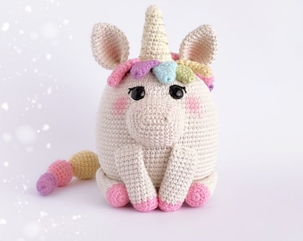 May include: A crocheted unicorn toy with a white body, pink hooves, and a rainbow mane. The unicorn has a long, pointed horn and a small, curled tail.