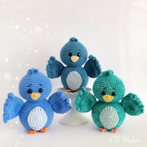 May include: Three crocheted bird toys. One is blue, one is light blue, and one is teal. They are all sitting on a white surface.