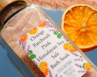Puede incluir: Un tarro de vidrio lleno de baño de sal del mar muerto rosa del Himalaya. La etiqueta dice "Orange Patchouli Pink Himalayan Sea Salt Bath Soak" y "100% Natural Hecho con Aceites Esenciales".