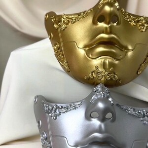 K&ouml;nnte beinhalten: Zwei dekorative Halbmasken. Eine ist goldfarben, die andere silberfarben. Beide Masken haben ein geformtes Gesichtsdesign mit Nase und Lippen. Aufwendige Schn&ouml;rkel verzieren die R&auml;nder und die Nase jeder Maske. Die Masken sind wahrscheinlich f&uuml;r eine Kost&uuml;mveranstaltung.