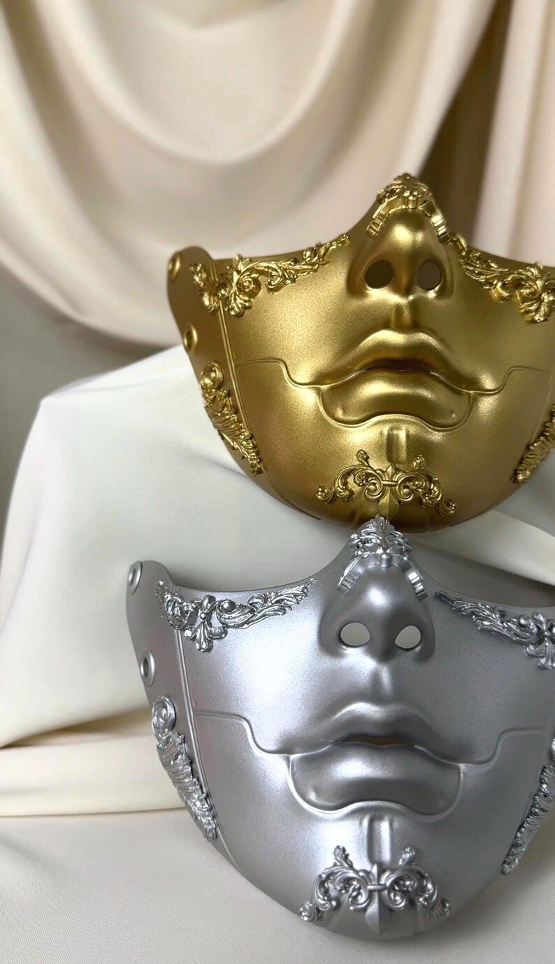 K&ouml;nnte beinhalten: Zwei dekorative Halbmasken. Eine ist goldfarben, die andere silberfarben. Beide Masken haben ein geformtes Gesichtsdesign mit Nase und Lippen. Aufwendige Schn&ouml;rkel verzieren die R&auml;nder und die Nase jeder Maske. Die Masken sind wahrscheinlich f&uuml;r eine Kost&uuml;mveranstaltung.