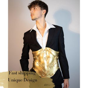 K&ouml;nnte beinhalten: Ein goldfarbenes, verziertes Kleidungsst&uuml;ck im Korsettstil mit floralem Design wird &uuml;ber einem wei&szlig;en Hemd und einer schwarzen Anzugjacke getragen. Das Bild enth&auml;lt den Text "Unique Design".