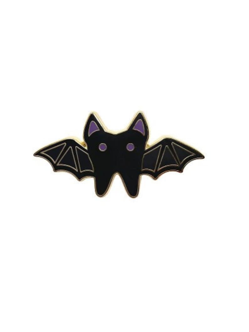 May include: A black enamel bat pin with purple eyes and gold accents. The bat has its wings spread out.
