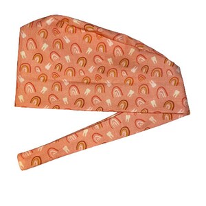 May include: A pink surgical scrub hat with a pattern of white teeth and multi-colored rainbows.