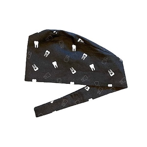May include: A black scrub cap with a white tooth pattern. The cap has a tie on the back.