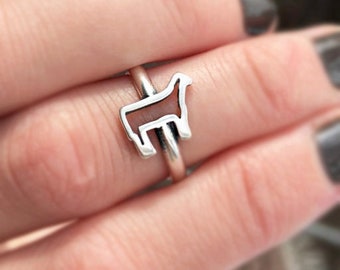 May include: A silver ring with a cutout design of a cow. The ring is worn on a finger.