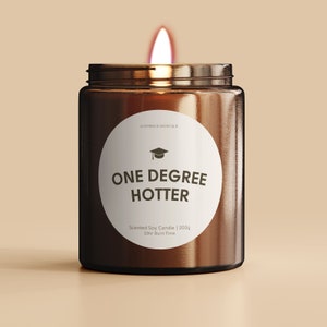 May include: A brown glass candle jar with a white label that says "One Degree Hotter" and features a graduation cap icon. The label also says "Scented Soy Candle | 200g | 33hr Burn Time".